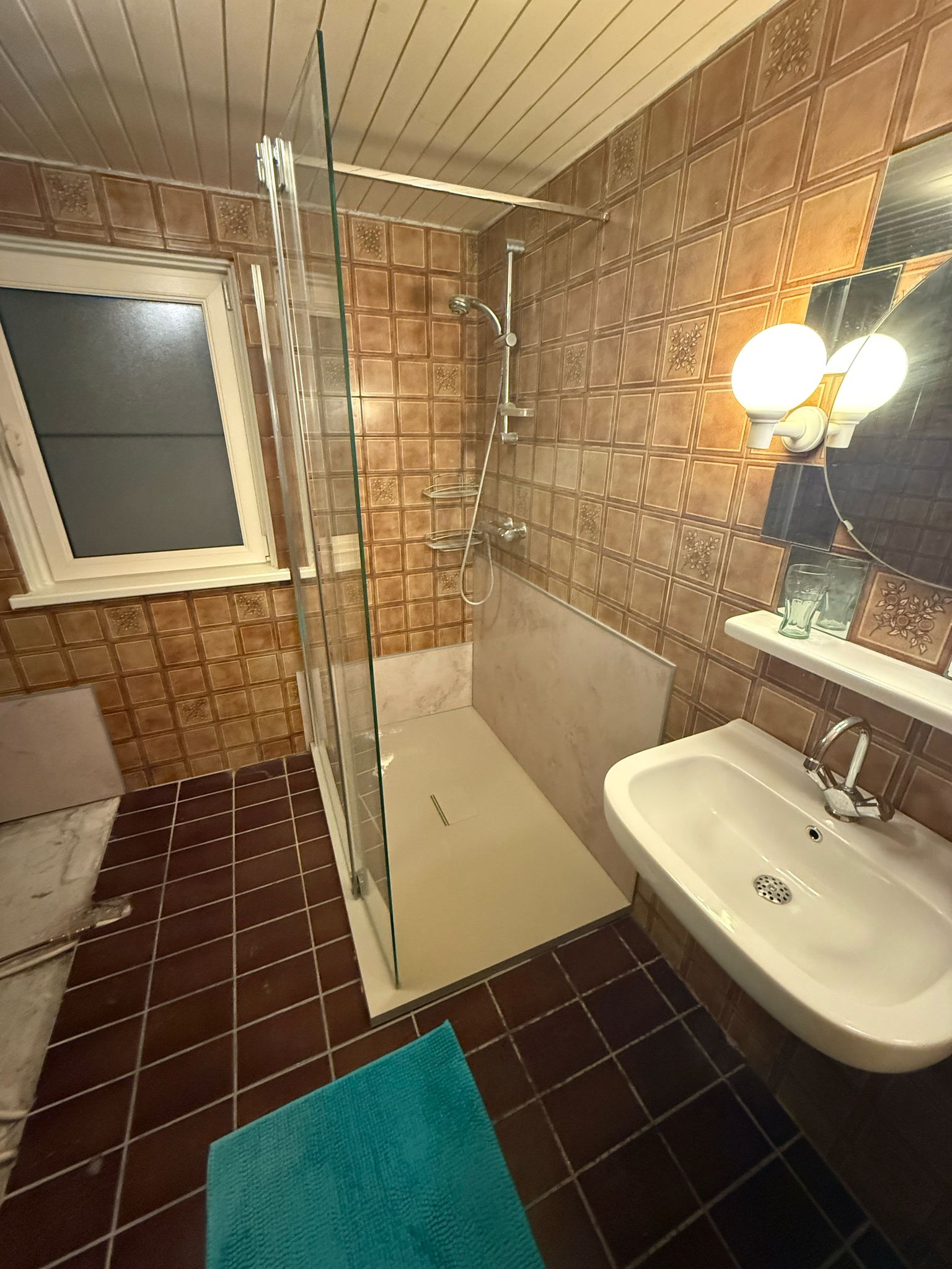 Badkamer met bruine tegels, douche, wastafel en toilet