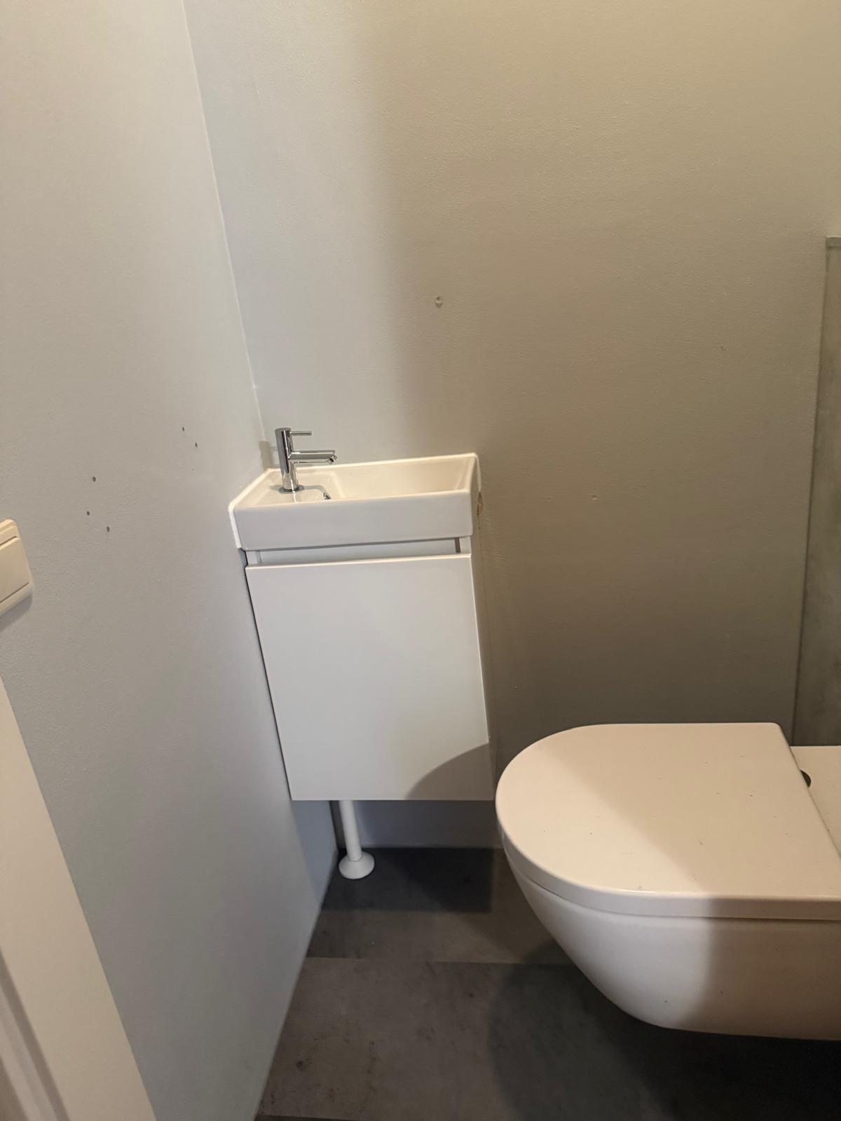 Wit betegelde badkamer met toilet en wastafel