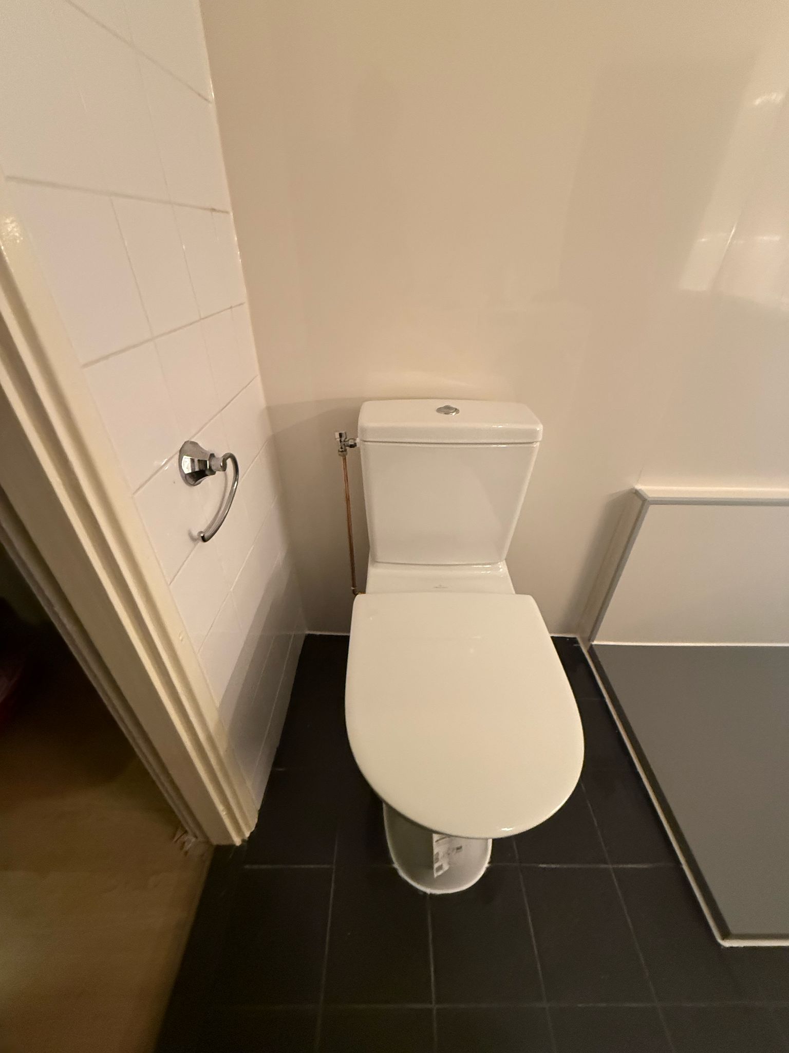 Wit toilet in badkamer met witte tegelwand en zwarte vloer