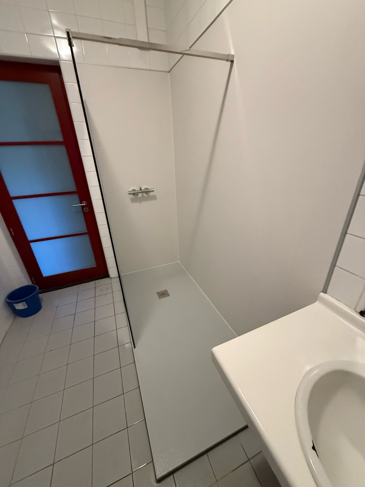Wit betegelde badkamer met glazen douchewand en witte wasbak
