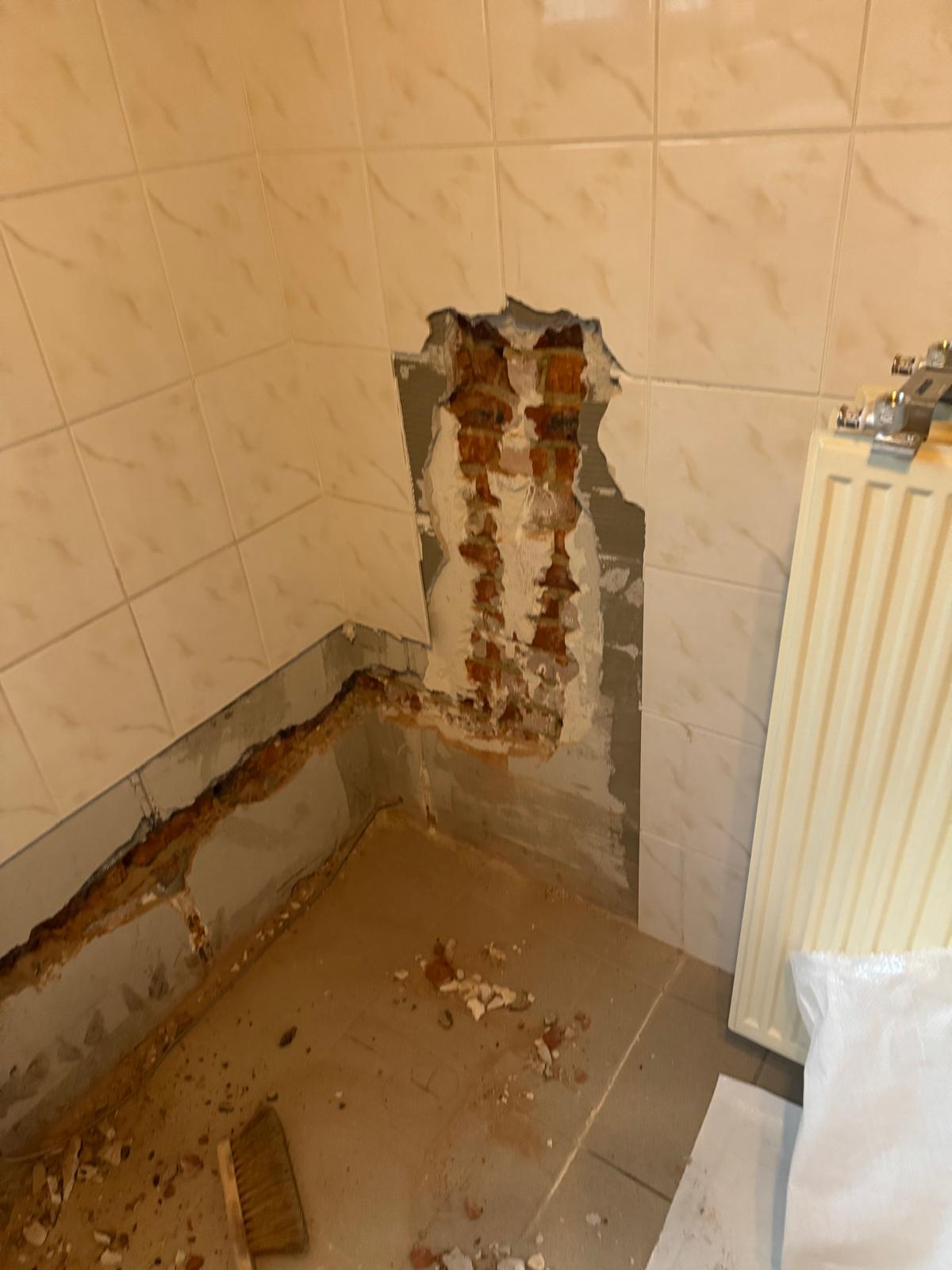 Gat in de badkamerwand met zicht op rode stenen en grijze specie
