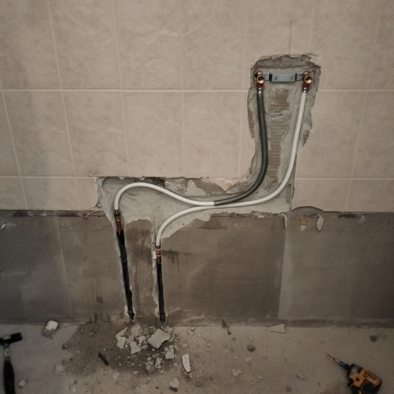 Sleuf in badkamerwand met blootgelegde waterleidingen en elektriciteitskabels