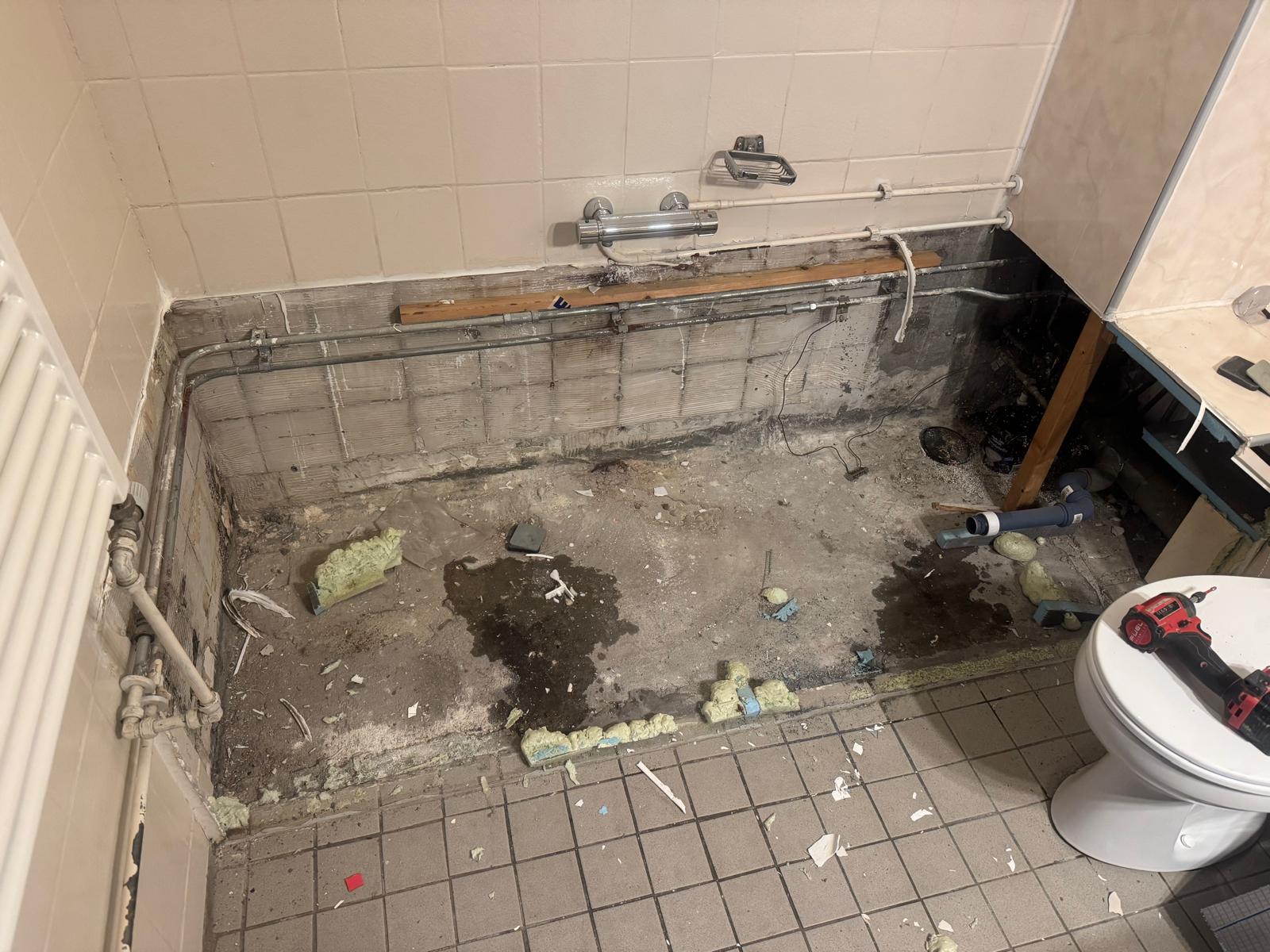 Slechte staat badkamer met oude betegeling en rioleringswerkzaamheden
