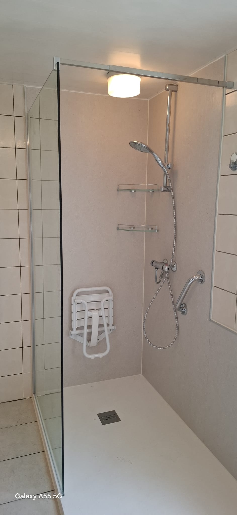 Douchecabine met glazen wand, witte tegelvloer en beige wanden, toegankelijk