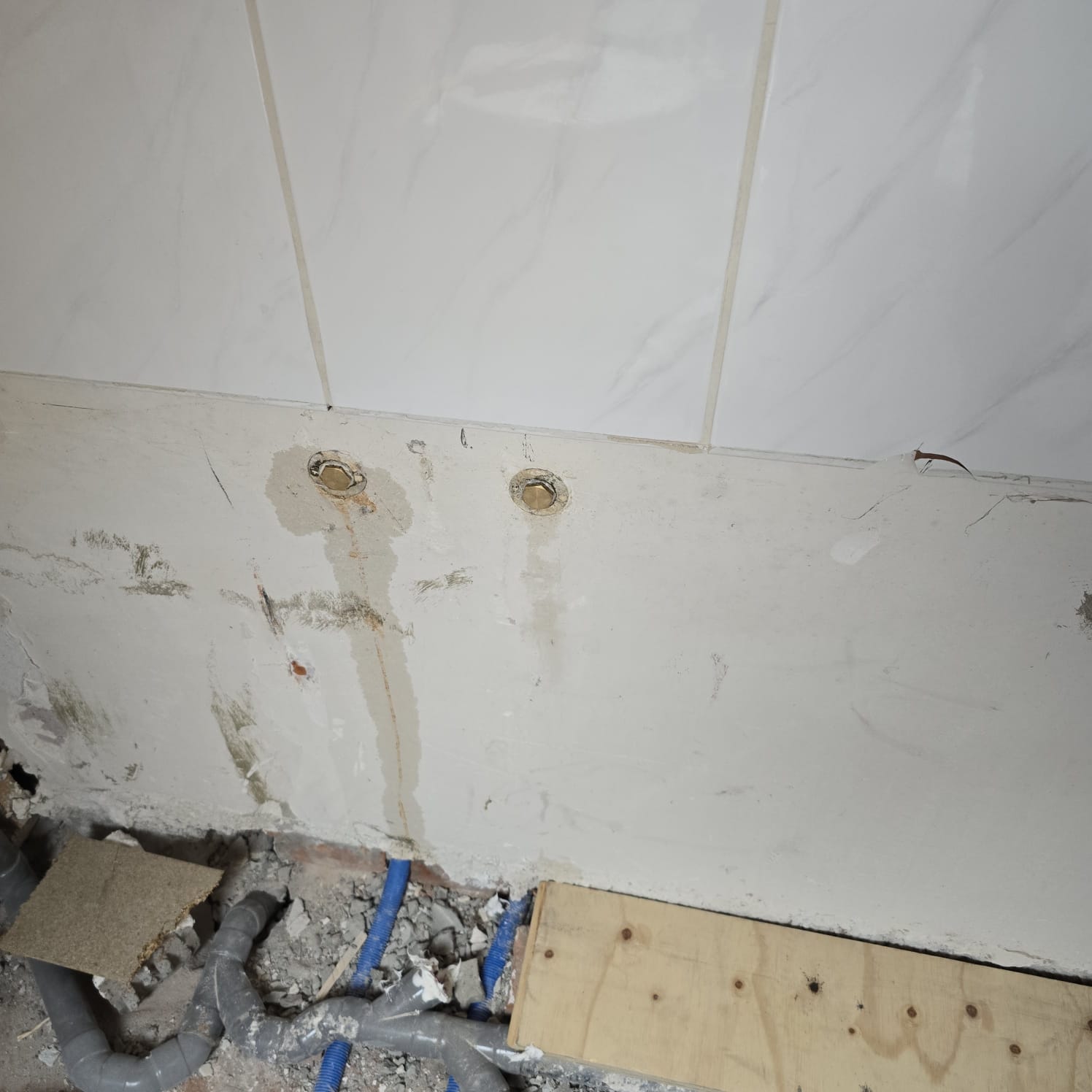 Sleuf in badkamerwand met blootgelegde leidingen en marmeren betegeling