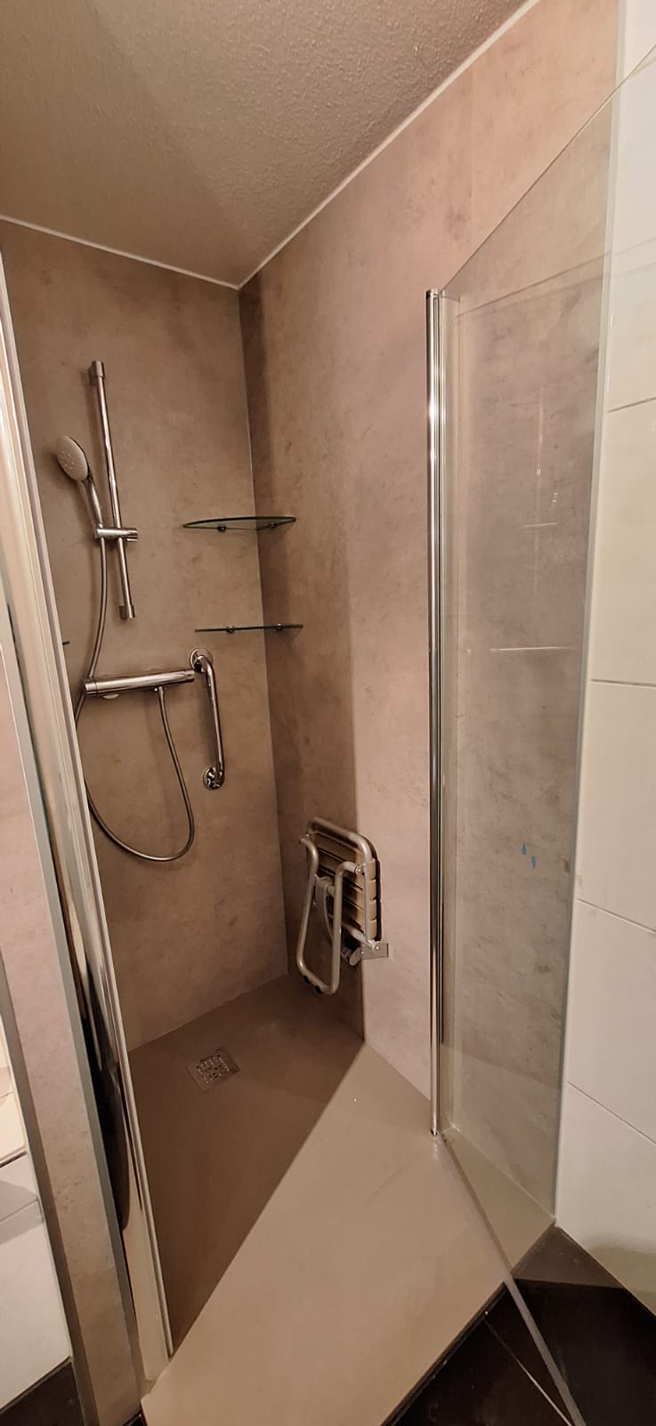 Douchecabine met glazen deur en beige betegeling, metalen douchekop en greep