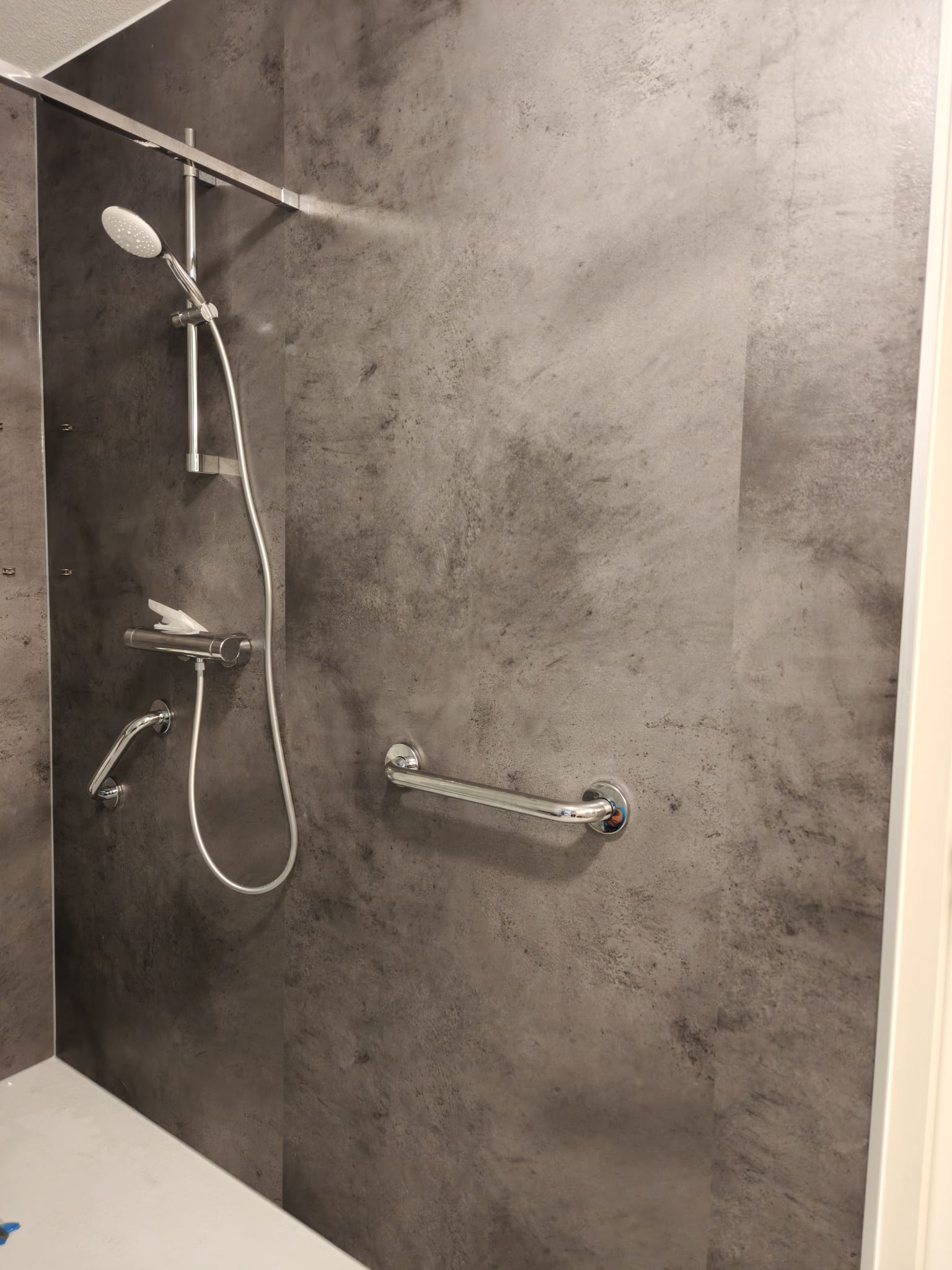 Douche met grijze wandtegels en een vaste douchekop en greep