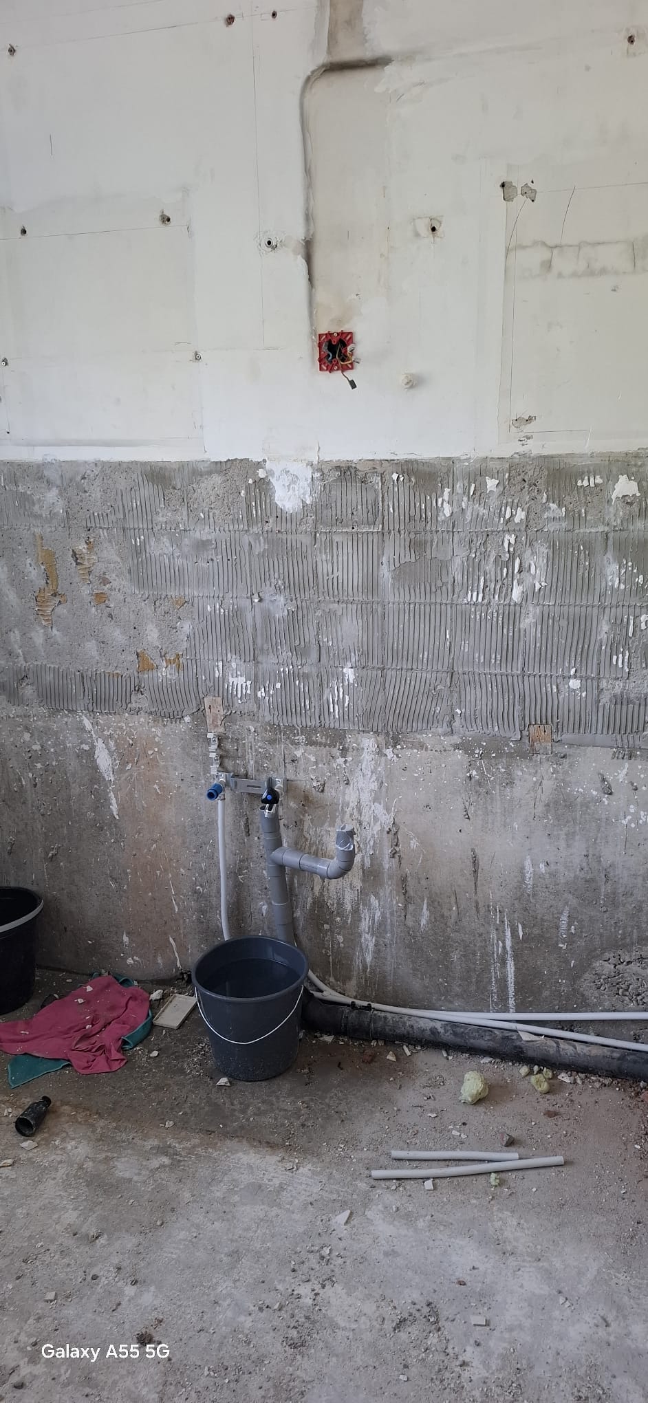 Slechte staat badkamer tijdens renovatie met zicht op de betegelde onderkant muur en waterleidingen