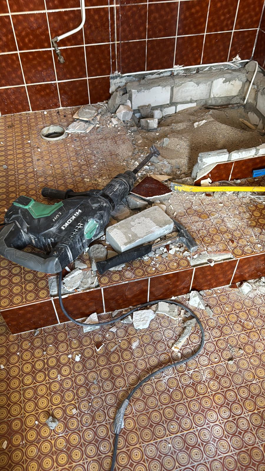 Sloopwerkzaamheden in badkamer met rode tegelvloer en -wanden, gereedschap aanwezig