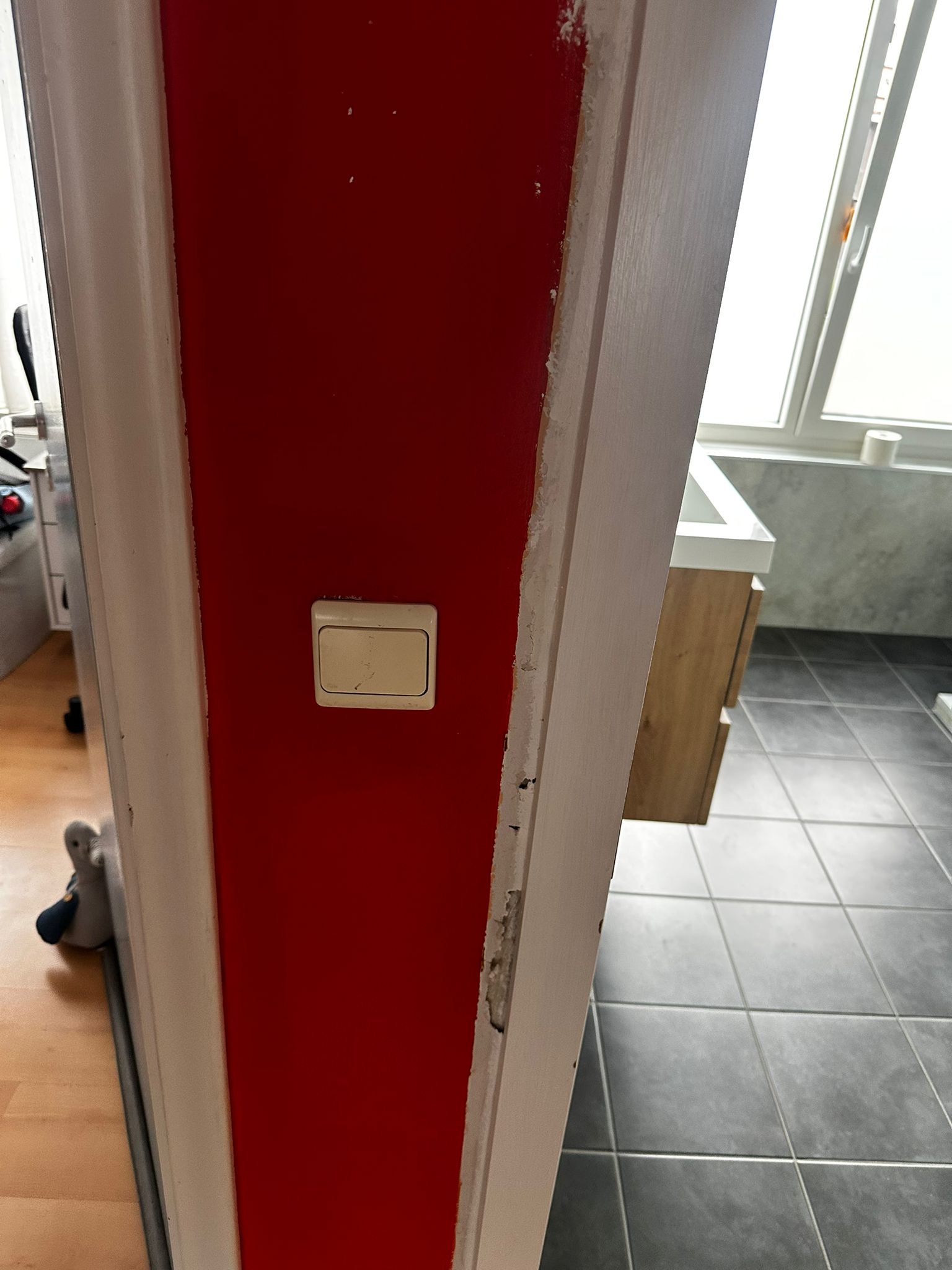 Deur naar badkamer met rode deur en witte deurlijst, grijze tegelvloer en wasbak