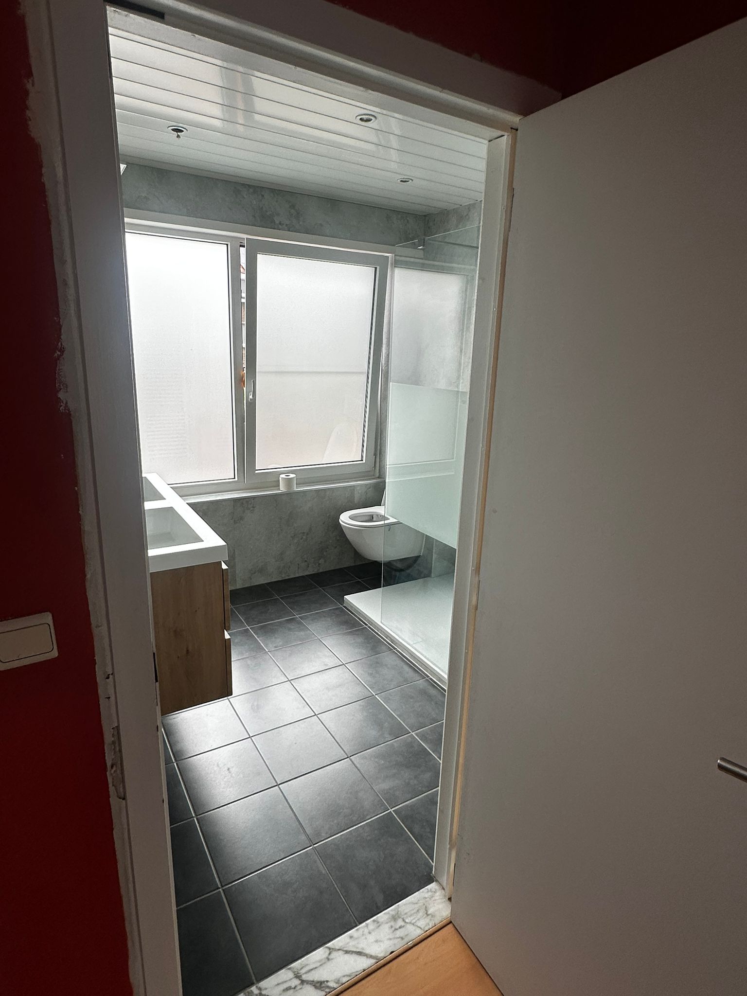 Badkamer in renovatie, grijs en wit interieur met zwarte vloer en houten meubel