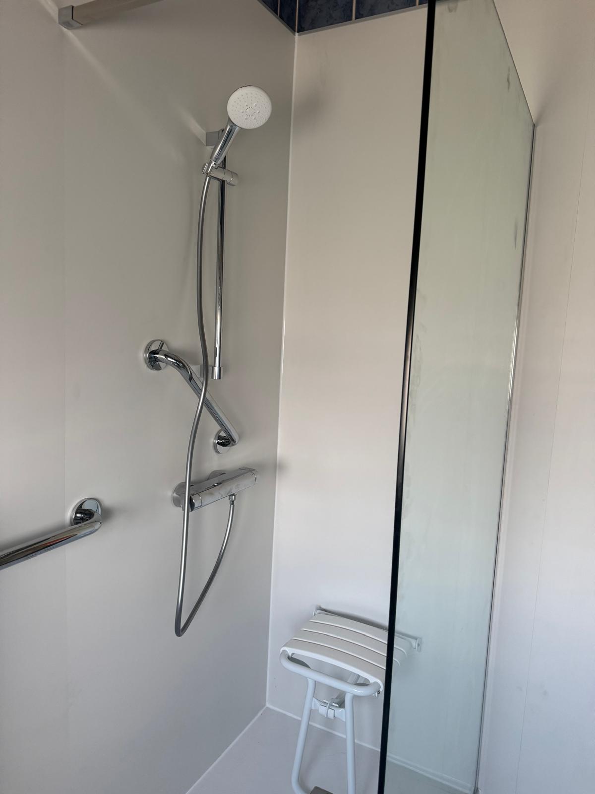 Douche met glazen deur, witte wanden, chroomkranen en stoel voor toegankelijkheid