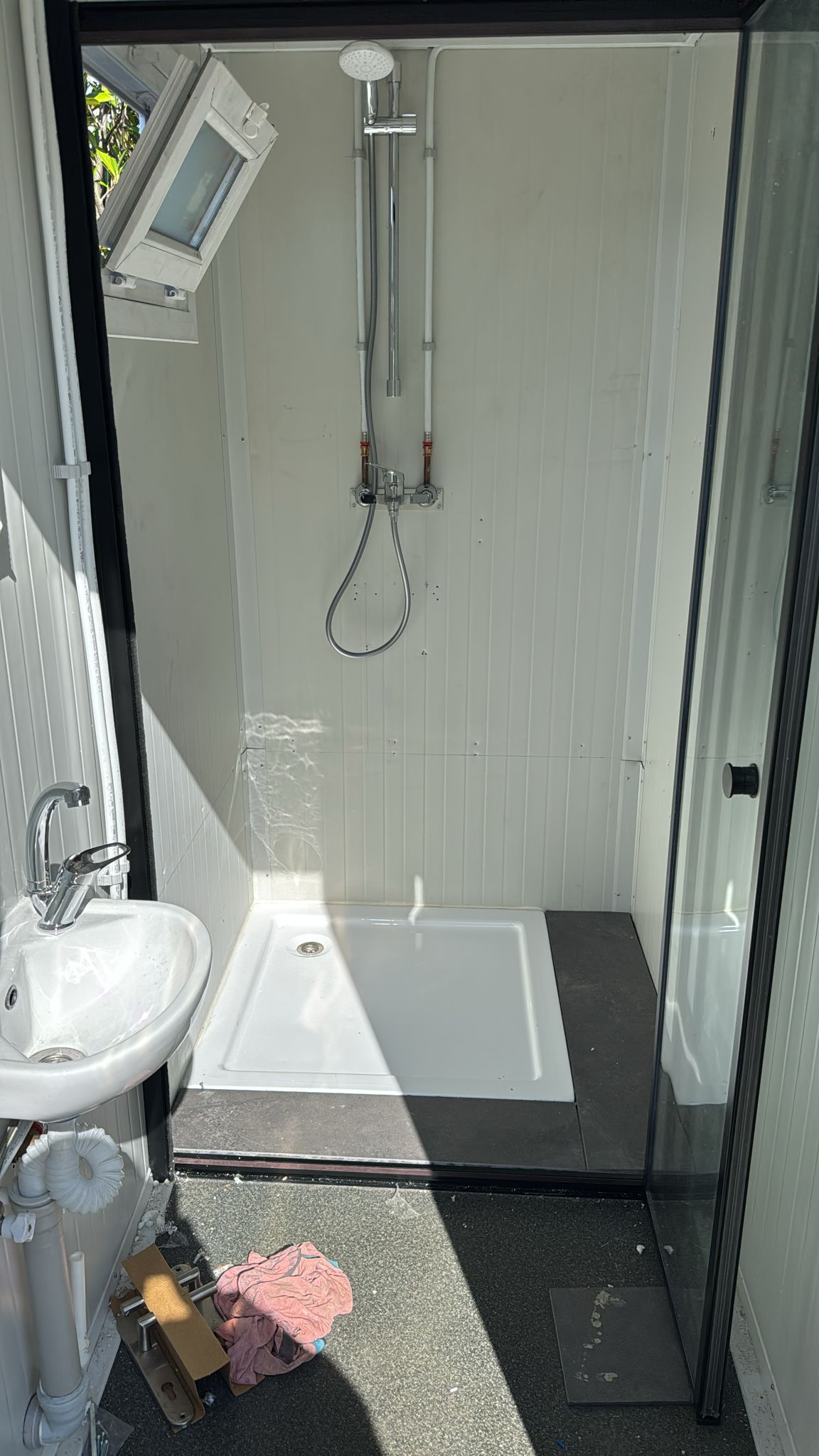 Badkamer met witte douche, wastafel en donkere vloer tijdens renovatie