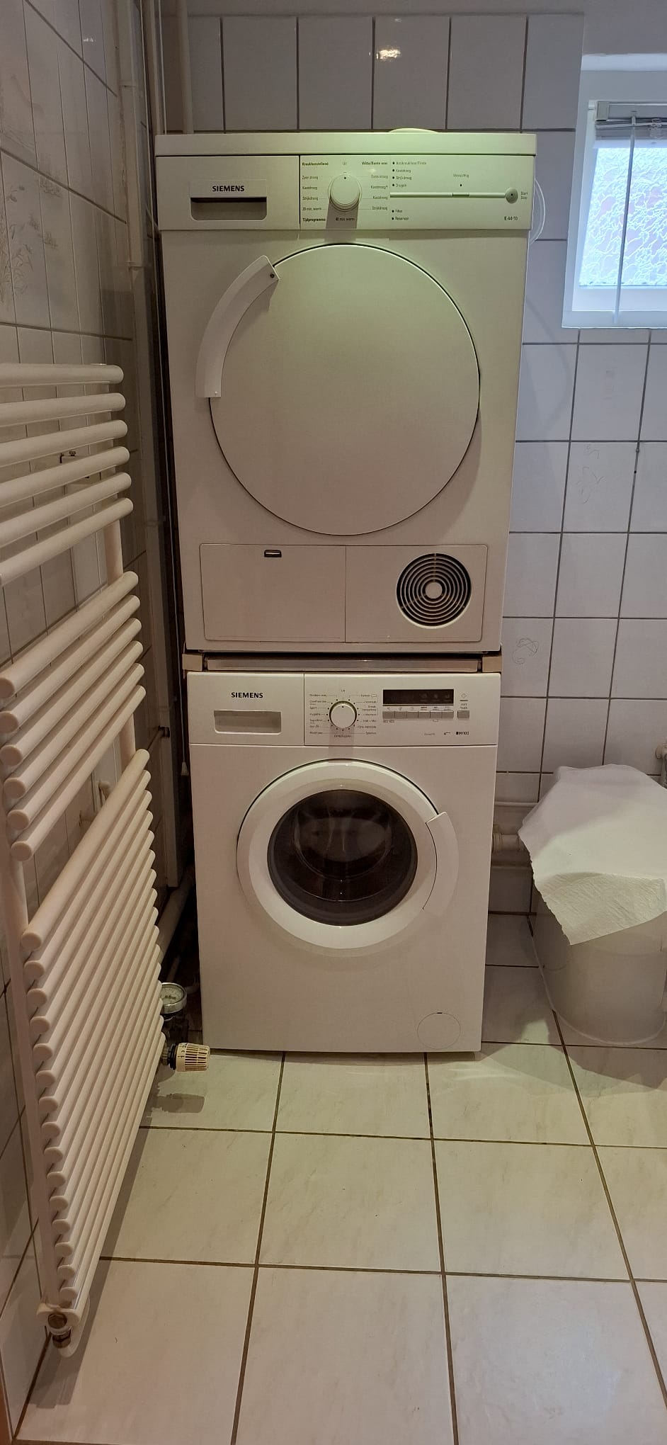 Wit betegelde badkamer met wasmachine en droger op elkaar gestapeld