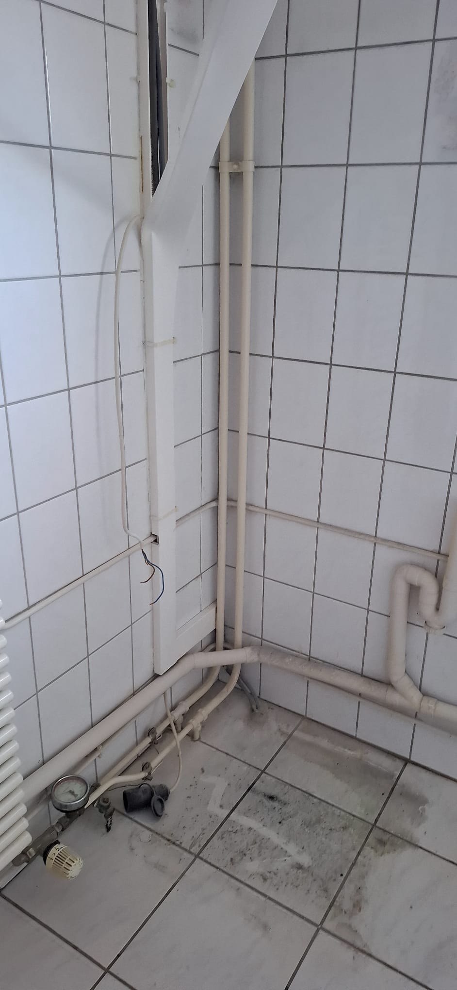 Slechte staat badkamer met witte tegelwanden en -vloer en zichtbare leidingen