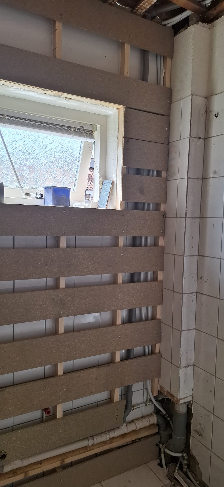 Badkamer in renovatie, houten panelen voor betegeling, blootgelegde leidingen en oude tegels