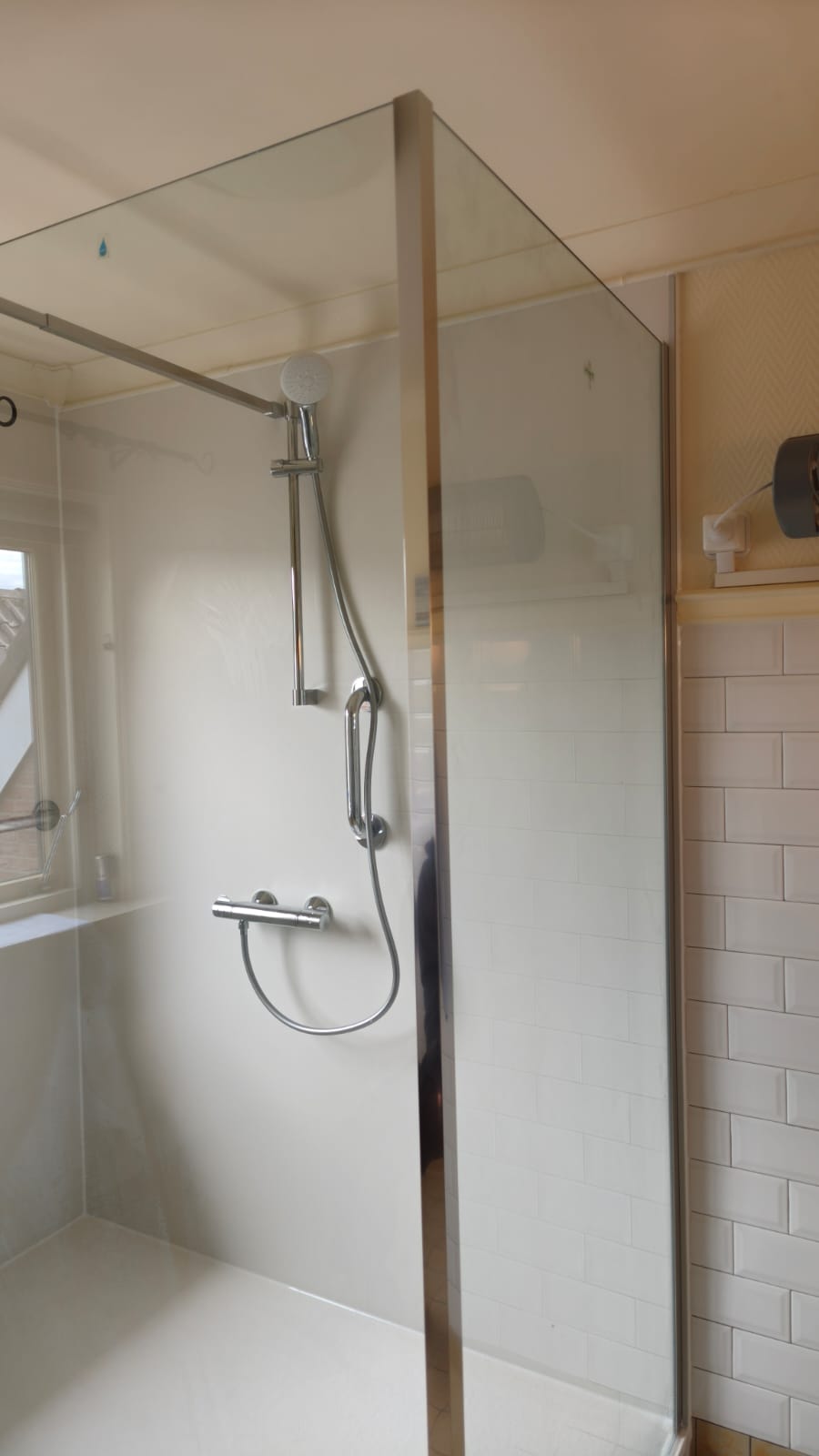 Douchecabine met glazen wand en chroom douchekraan in witte tegelbadkamer