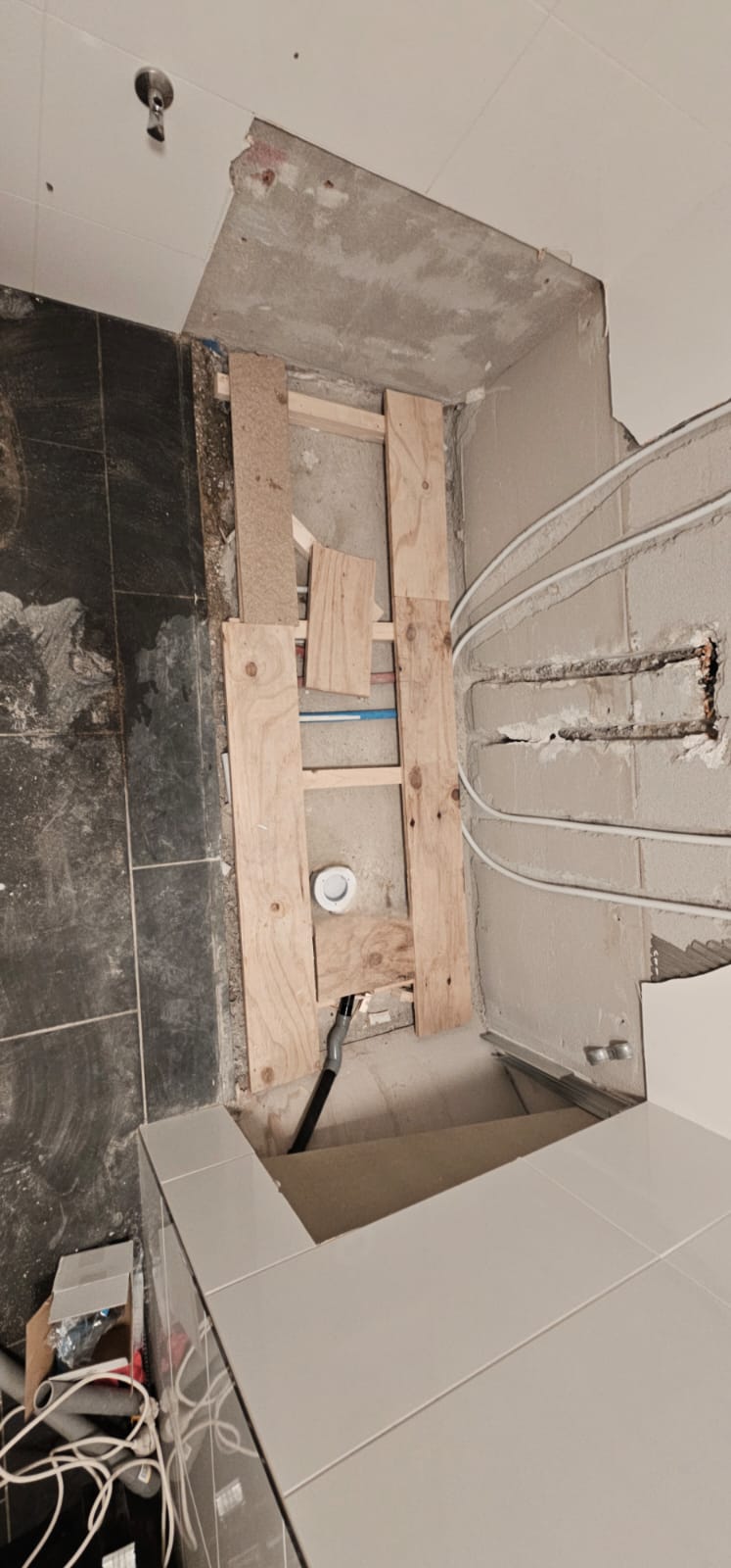 Badkamer renovatie in uitvoering, houten constructie en grijze tegels