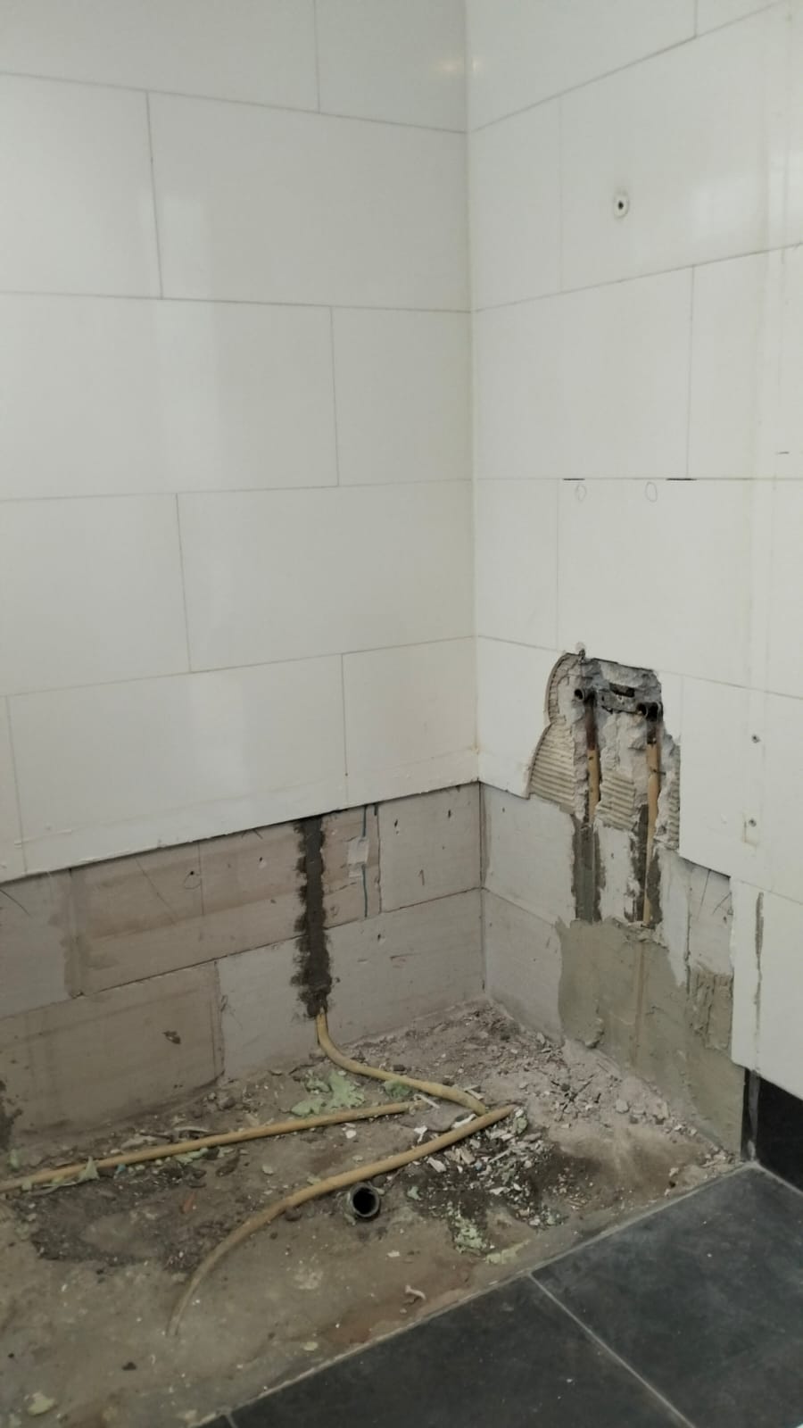 Slechte staat badkamer met kapotte tegelwand en leidingen