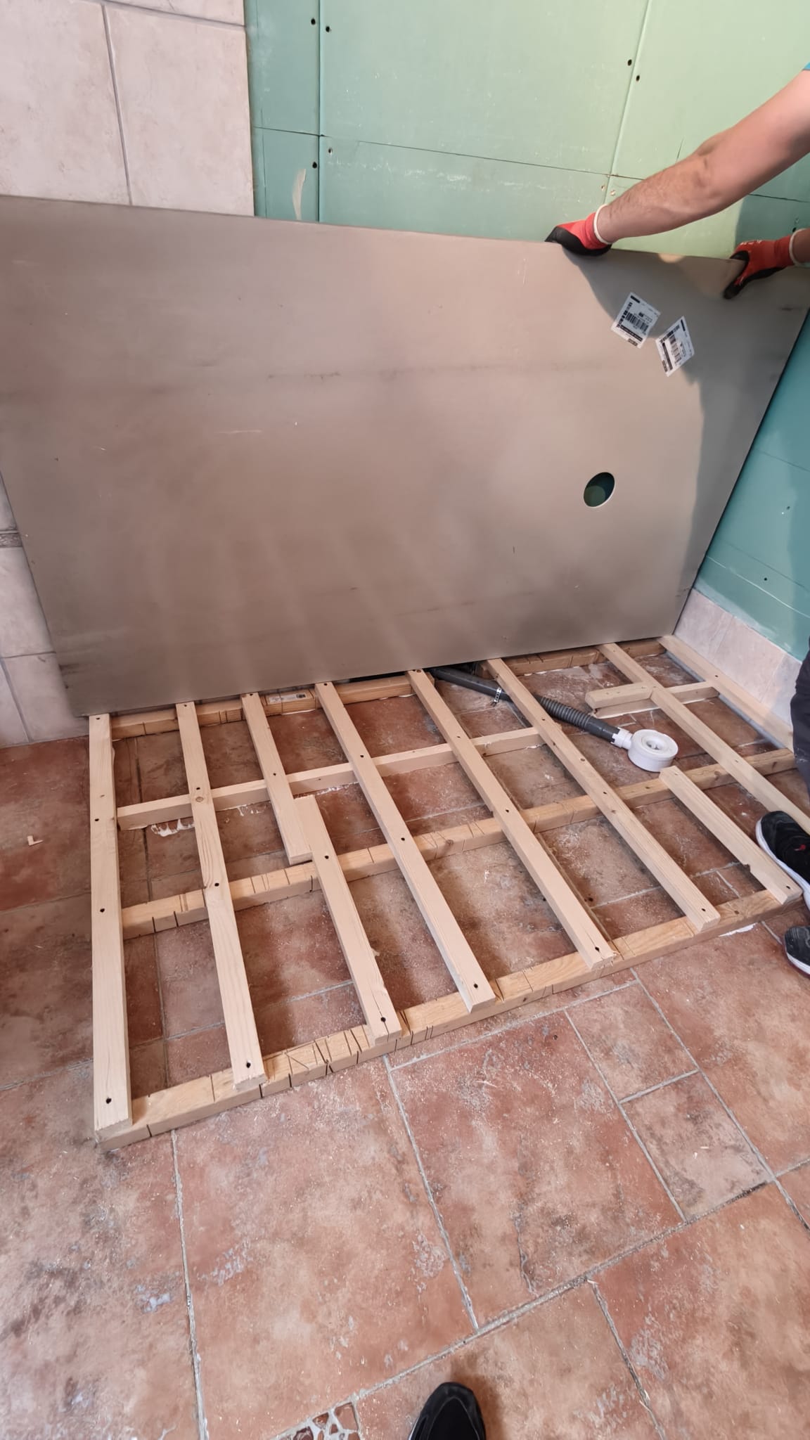Een persoon plaatst een grote plaat tegen een muur in een badkamer tijdens renovatie