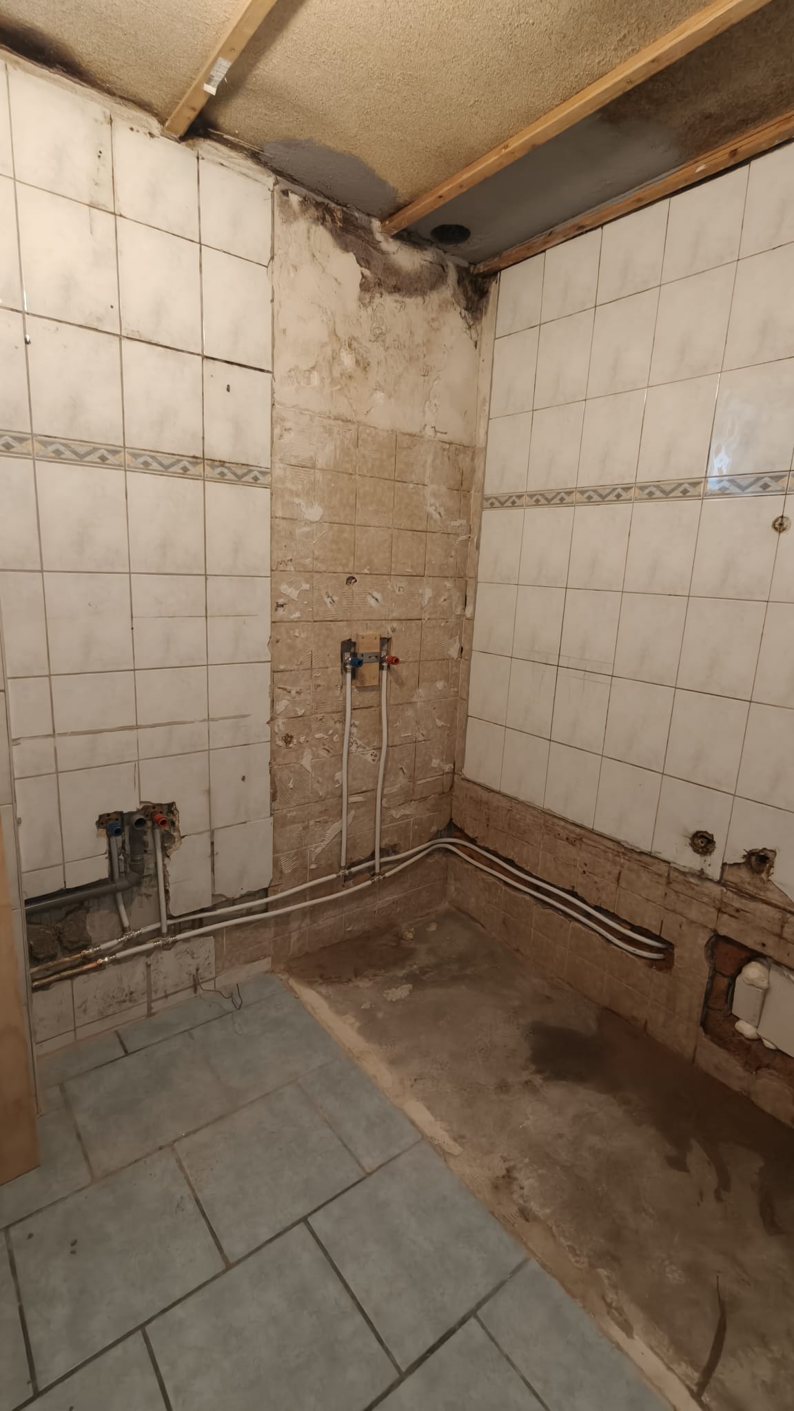 Slechte staat badkamer met beschadigde tegels en zichtbare leidingen