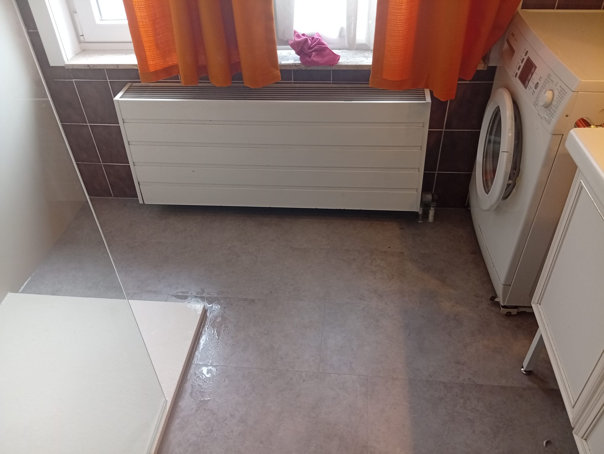 Grijze tegelvloer en bruine wandtegels in kleine badkamer met wasmachine en radiator