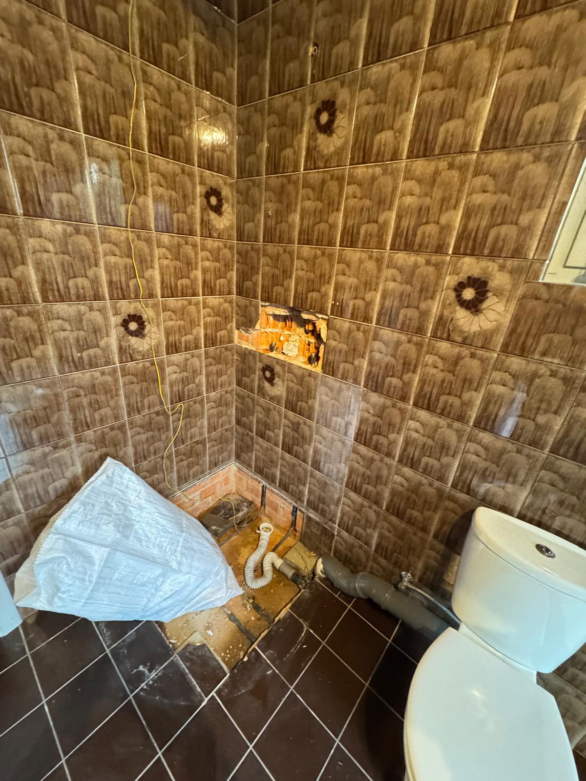 Slechte staat badkamer met bruine tegels en kapotte douche