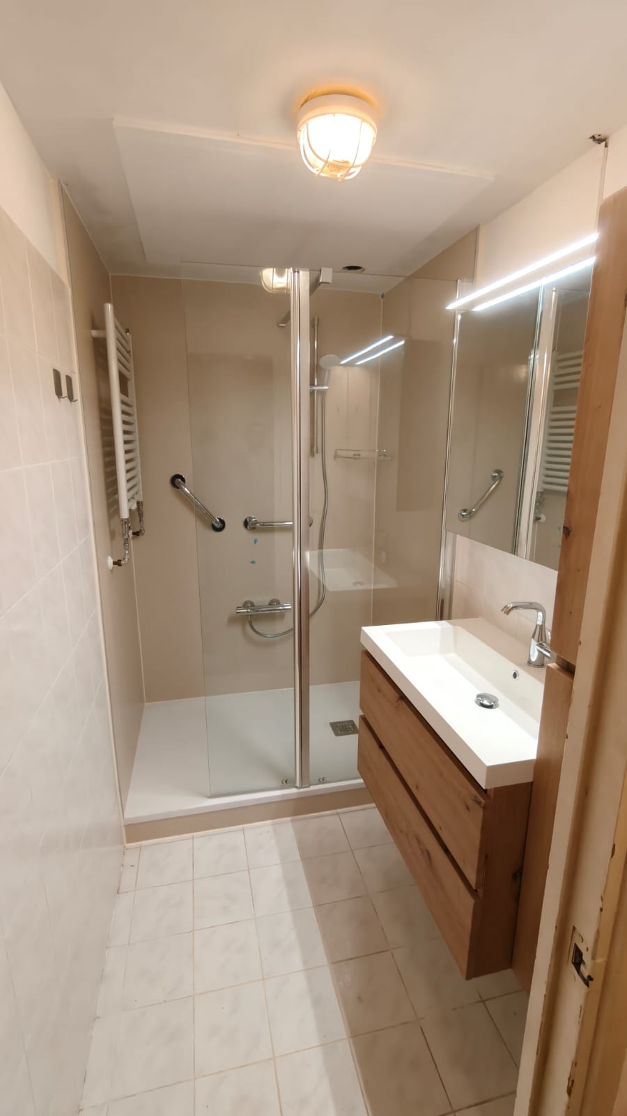 Badkamer met beige tegels, douche, wastafel en spiegel